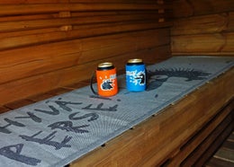 Refroidisseurs de canette orange et turquoise Le H&eacute;risson Juron sur une serviette pour banc de sauna Hyv&auml; perse.